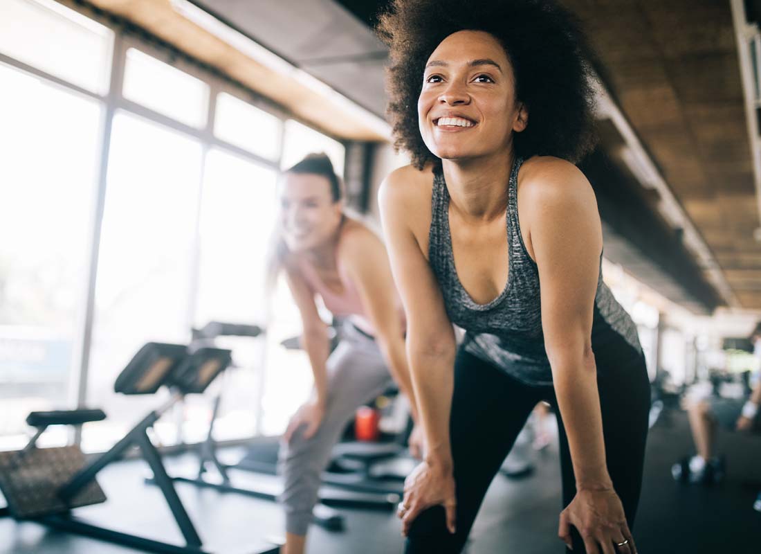 Fitness Center Insurance - Young Woman Exercising and Catching Her Breath While Training at Fitness Club with Exercise Equipment in the Distance