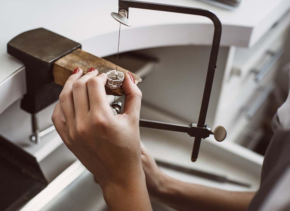 Jewelers Insurance - Close-up of a Young Female Jeweler’s Hands Working on a New Silver Ring at Her Workbench